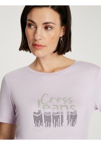 Jasnofioletowa koszulka z krótkim rękawem z napisem "Cross Jeans" w zielonej i czarnej kropki, teksturowana efektem gradientu.