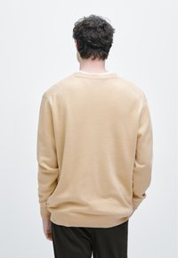 Béžový svetr s dlouhými rukávy a kulatým výstřihem, vyrobený z měkkého, strukturovaného materiálu. Prošívání na ramenou, bez vzorů.