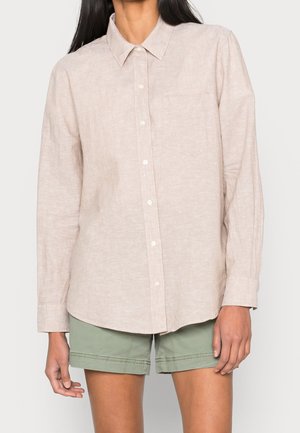 Beige Leinenhemd mit Button-Down-Kragen, Brusttasche und subtiler Textur. Getragen mit grünen Roll-Up-Shorts.