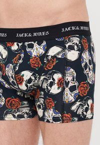 Baumwollboxershorts mit dunkelblauem Grundton, verziert mit einem bunten Muster aus Schädeln und Rosen. Elastischer Bund mit "JACK & JONES"-Markenlogo in Weiß.