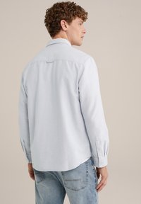 Chemise bleu clair à manches longues, avec un col et un ourlet en queue. Fabriquée dans un tissu doux avec une texture unie. Design décontracté.