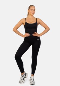 Czarny elastyczny zestaw odzieży sportowej, w skład którego wchodzi dopasowany top na cienkich ramiączkach oraz legginsy z wysokim stanem, oba o gładkiej fakturze i minimalnym logo.