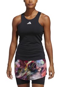 Zwart sporttop zonder mouwen met wit logo, gecombineerd met een kleurrijke meshrok met bloemenpatronen en een accentonbroekje eronder.