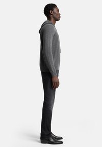 Grauer Kapuzenpullover aus weichem Stoff, mit einer Vordertasche und Kordelzug. Kombiniert mit dunklen Jeans und schwarzen Lederstiefeln.