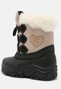 Schneestiefel mit einem beigefarbenen Obermaterial und einem glitzernden Herzdetail, schwarzer Gummisohle und einem flauschigen, cremefarbigen Futter an der Oberkante.