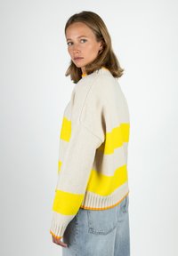 Cremefarbener Pullover mit auffälligen gelben Streifen und einem orangen gerippten Saum. Weiche Textur und lockere Passform, mit überschnittenen Schultern und einem runden Ausschnitt.