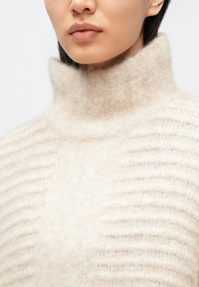 Kremfarvet rullekravesweater med blødt, tekstureret strik og lodrette ribdetaljer, med høj krave og afslappet pasform.