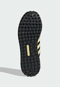 Μαύρη σόλα παπουτσιού από καουτσούκ με έντονες στρογγυλεμένες εξοχές, διαθέτει τρεις διαγώνιες ρίγες και μια χρυσή πλακέτα με ανάγλυφο λογότυπο.