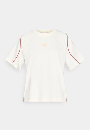 White t-shirt with short raglan sleeves, featuring red stitching along the shoulders and a small beige logo on the chest. Soft fabric texture.