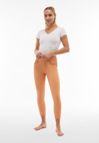 Leggings color pesca con una texture liscia, vita alta e design aderente, abbinati a una maglietta bianca a maniche corte.