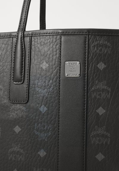 Borsa tote in pelle nera MCM con superficie texturizzata, striscia verticale in pelle e targhetta del marchio in argento con viti e numero di serie.
