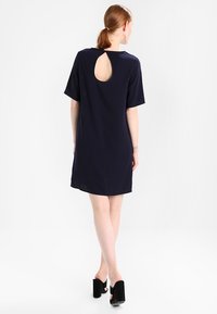 Námořnické modré šaty s krátkým rukávem, které mají výřez ve tvaru klíče na zádech. Vyrobené z měkké, lehké látky, ke kolenům s hladkým povrchem.