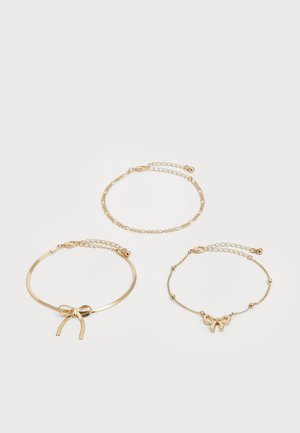 Three delicate gold chain bracelets, one with a bow charm, one with a bow-shaped band, and one with small linked ovals.