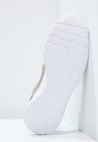 Sula av en vit Nike-sneaker med ett fyrkantigt mönster, vinklad mot ett vitt vägg- och golvhörn.