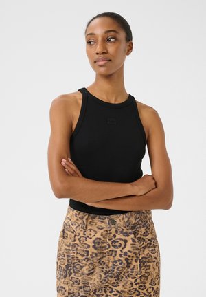 Top nero senza maniche con una superficie a coste e scollatura rotonda, abbinato a una gonna beige con stampa leopardata, dotata di tasche e chiusura con bottone.