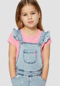 Lichtblauwe denim overall met froncende schouderbanden, gecombineerd met een roze t-shirt; heeft geborduurde bloemaccenten en zakken.