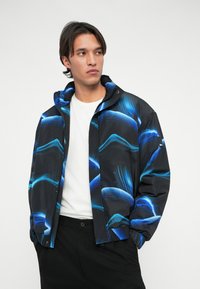 Čierna bunda s modrými abstraktnými vzormi, so zipsom a stojacím golierom. Obsahuje elastické manžety a postranné vrecká. Nosená cez bielu košeľu.
