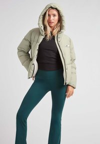 Lys grøn pufferjakke med hætte, der har en frontlynlås og knaplukning, parret med høj talje mørkegrønne leggings.