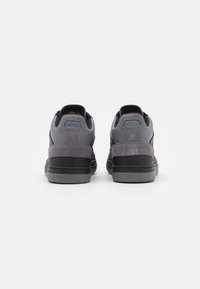 Mustat ja harmaat lenkkarit, joissa on teksturoitu mokkanahkainen kantapää ja sileä yläosa, takana olevan logoplaatin ja kestävän kumipohjan kera.