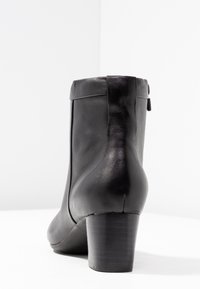 Stivaletto alla caviglia in pelle nera con texture liscia, caratterizzato da punta arrotondata e tacco medio a blocco; chiusura posteriore con zip visibile.