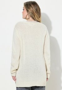 Pull crème long et ample avec une texture en maille épaisse, des poignets côtelés et un ourlet légèrement allongé à l'arrière.
