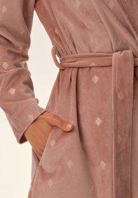 Różowy pluszowy szlafrok charakteryzuje się miękką teksturą, wzorem w diamenty, paskiem w talii oraz bocznymi kieszeniami. Materiał wygląda na przytulny i gładki.