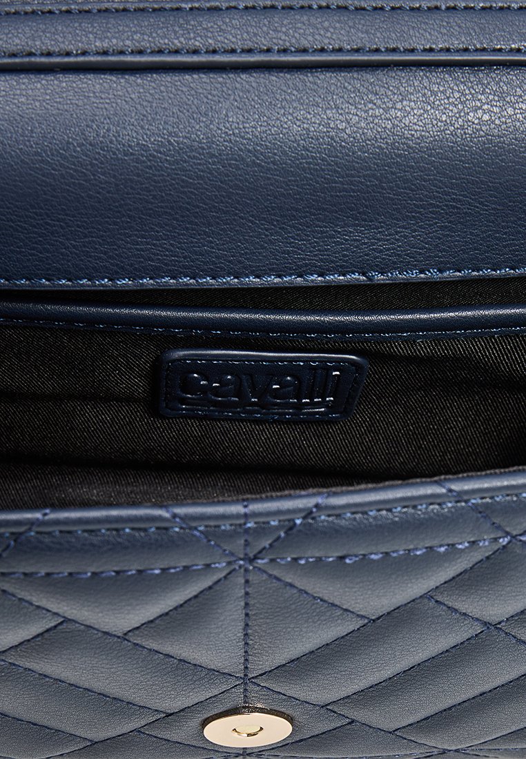 Interior de bolsa de cuero azul marino con patrón acolchado, presenta un forro de tela negra y una etiqueta de logo. Detalle de hardware dorado en la base.