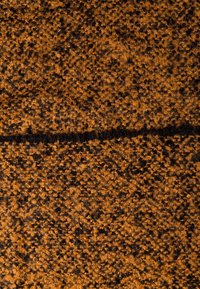 Gros plan sur un tissu en laine orange et noire texturé avec une ligne horizontale plus foncée traversant le milieu.