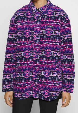 Fialová, růžová a tmavě modrá fleece košile s knoflíkovou přední částí, límcem, náprsní kapsou a dlouhými rukávy, nošená osobou v černých kalhotách.