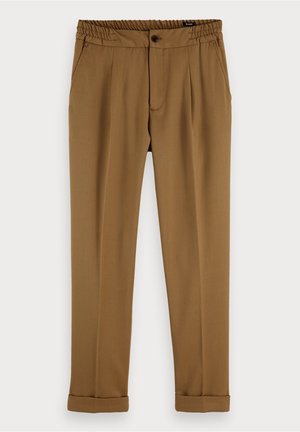 Pantalon marron sur mesure avec taille élastique, fermeture par bouton, poches latérales et revers pliés suspendu sur un fond blanc.