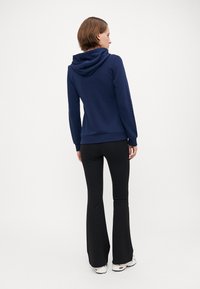 Marineblå hettegenser med lange ermer, ribbede mansjetter og kant. Kombinert med svarte vide bukser og hvite joggesko, viser et avslappet antrekk.