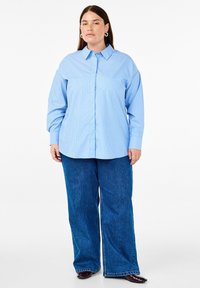 Camicia a righe blu e bianche con colletto, maniche lunghe e vestibilità rilassata, abbinata a jeans in denim blu a gamba larga.