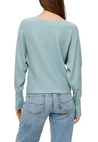 Hellblauer, gerippter Pullover mit weitem Ausschnitt und langen Ärmeln, kombiniert mit hochgeschnittenen Jeans aus hellblauem Denim. Strukturierte Stoffdetails sind sichtbar.