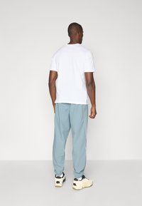 Hvit bomulls t-skjorte kombinert med lyseblå joggebukser, med elastiske mansjetter og sideaksenter. Brukt med hvite og svarte sneakers.