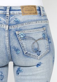 Ljusblå denimjeans med blommönster i akva och marinblått. Bakfickan är prydd med en detaljerad sömdesign och etikett.