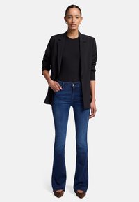 Blazer noir sur un top noir ajusté, associé à un jean flare bleu foncé. Les chaussures sont en imprimé animal marron avec un bout pointu.