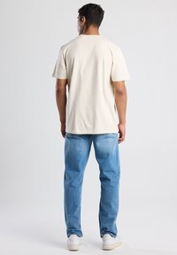 Beige puuvillane T-särk lühikeste varrukatega, lõdva lõikega, ümmarguse kaelusega. Kombineeritud heledate siniste teksade ja valgete tossudega.