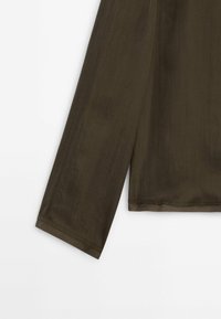 Haut à manches longues d'un vert olive foncé, présentant un tissu lisse légèrement transparent avec une coupe décontractée et un ourlet simple.