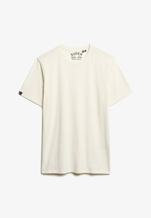 T-shirt en coton couleur crème avec des manches courtes, encolure ras du cou et une étiquette cousue sur la manche gauche. Texture lisse, design simple.