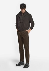 Mörkbrun huvtröja med scarfdetalj, i kombination med bruna byxor och svarta läderskor som framhäver en avslappnad look.