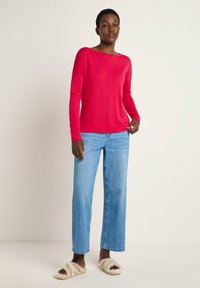 Red long-sleeve sweater, soft fabric, relaxed fit, crew neckline. Worn with light blue wide-leg jeans and fuzzy white slide sandals.