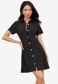 Black short-sleeve dress with a button-down front, featuring gold buttons, a collar, and a pleated skirt with a front slit.