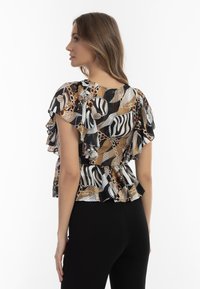 Sort og guld mønstret top med flæseærmer, peplum-design, der har zebrastriber og kædemotiver. Bæres med sorte bukser.