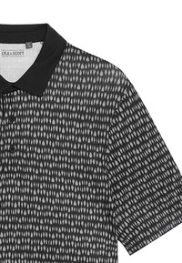 Svart polo tröja med ett geometriskt mönster i grått. Utmärkande delar inkluderar en svart krage och knappslå.