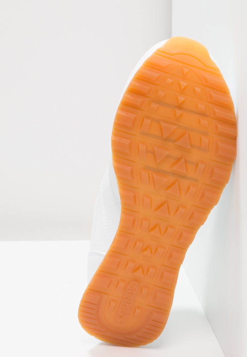 Witte sneaker met een gestructureerde oranje rubberen zool, met een zigzagpatroon. Het bovenwerk is gemaakt van glad synthetisch materiaal en heeft witte stikselaccenten.