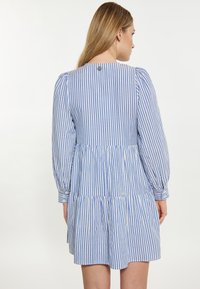 Abito a righe blu e bianche con design a strati, maniche lunghe a sbuffo e dettaglio con bottoni sulla schiena. Realizzato in tessuto leggero.