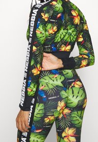 Setti aktiivivarusteita trooppisella printillä mustana, jossa on vihreitä lehtiä, värikkäitä kukkia ja tukkasauruksia. Mukana merkkipojat hihoissa ja leggingeissä.