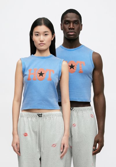 Top cropped azul com as palavras "HOT" e estampa de estrela. O tecido é algodão macio. A modelo usa calças de treino cinza claro com detalhes de estampa de lábios.