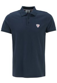 Námořnická modrá polo košile vyrobená z bavlny. Obsahuje límec, tříbuttonový zapínací límec a malou vyšívanou nášivku na levé straně hrudi.