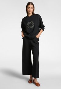 Svart sweatshirt med en texturerad blommönsterdesign på bröstet, kombinerad med vida svarta byxor och bruna ballerinas. Slätt tyg, avslappnad passform.